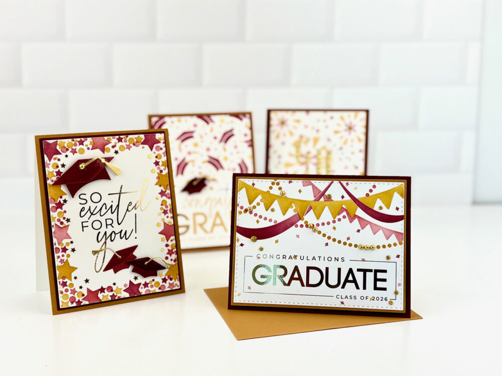 Colorful graduation cards on a white surface, with the front card reading 'GRADUATE' and 'CONGRATULATIONS' amid bunting and confetti designs.