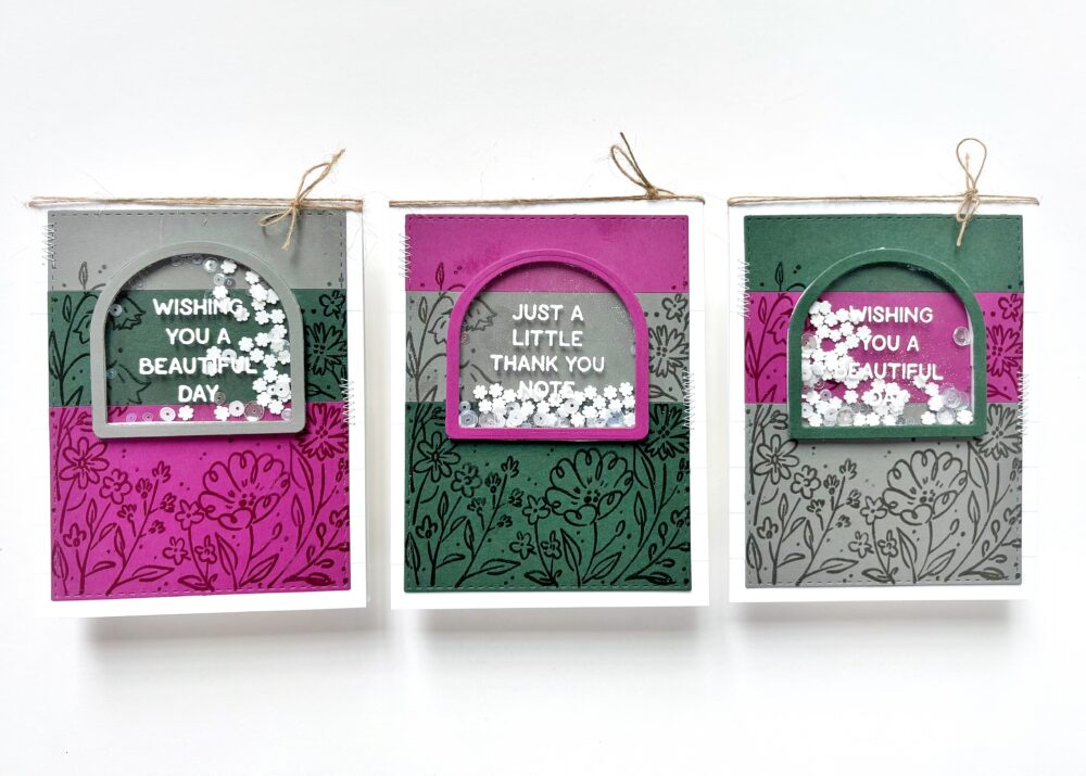 Three hanging decorative cards with floral patterns and circular window panels. Left card (gray/pink) reads 'WISHING YOU A BEAUTIFUL DAY'; middle card (pink) reads 'JUST A LITTLE THANK YOU NOTE'; right card (green) reads 'WISHING YOU A BEAUTIFUL DAY'.