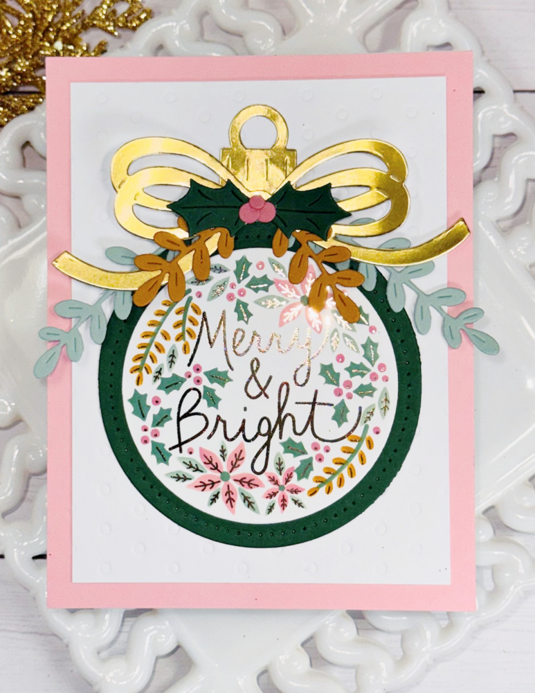 Festive Christmas card with a wreath, gold ribbon, holly, and pink border, reading 'Merry & Bright'.
