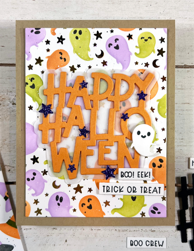 Halloween card with orange cutout letters spelling 'HAPPY HALLOWEEN' against a ghost and star pattern background of purple, green, orange ghosts and black stars.